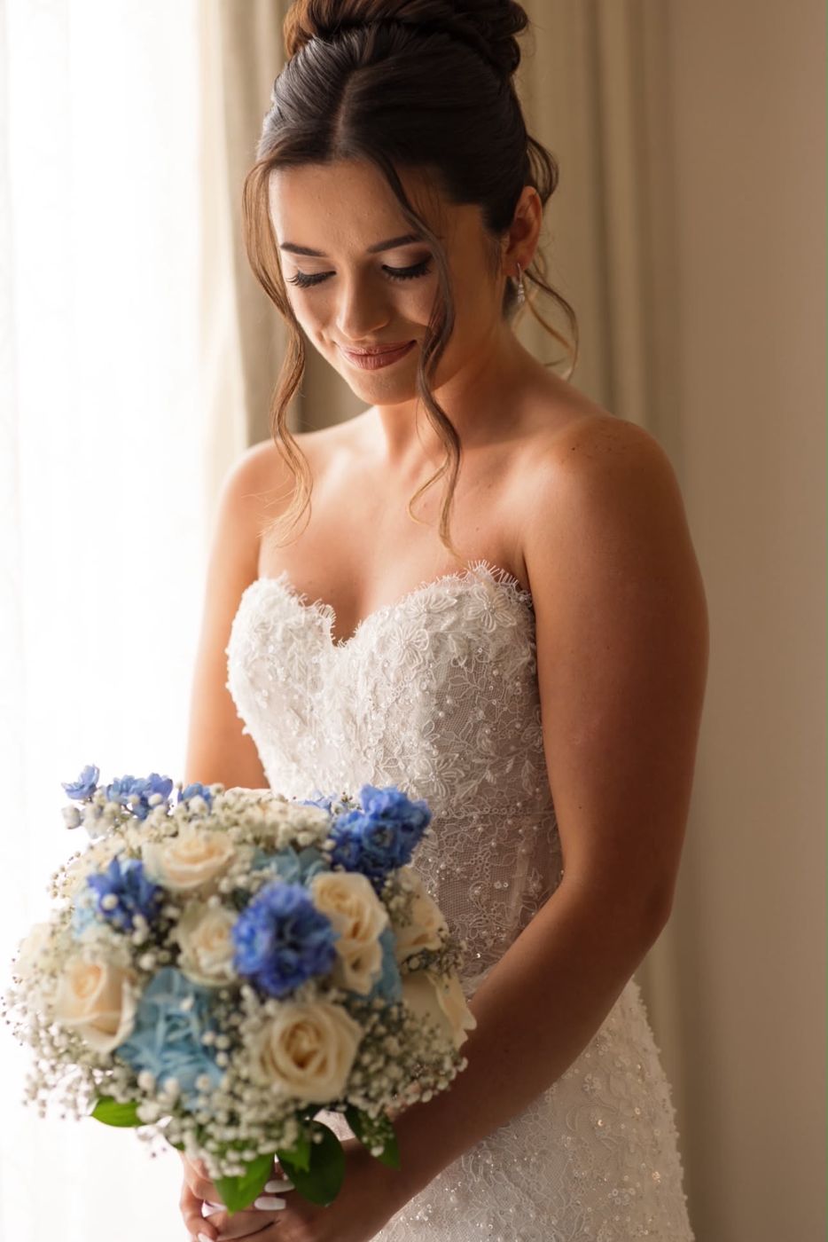 Bride in a strapless lace gown looking down at her blue and ivory bouquet