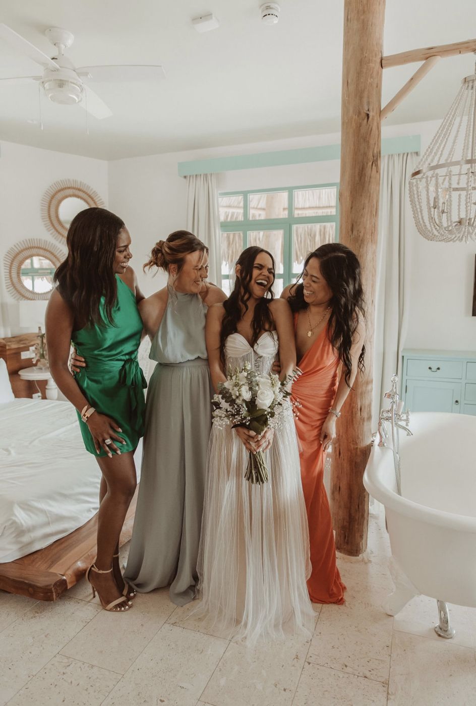 Laughing bride with her bouquet among bridesmaids in green, sage and coral