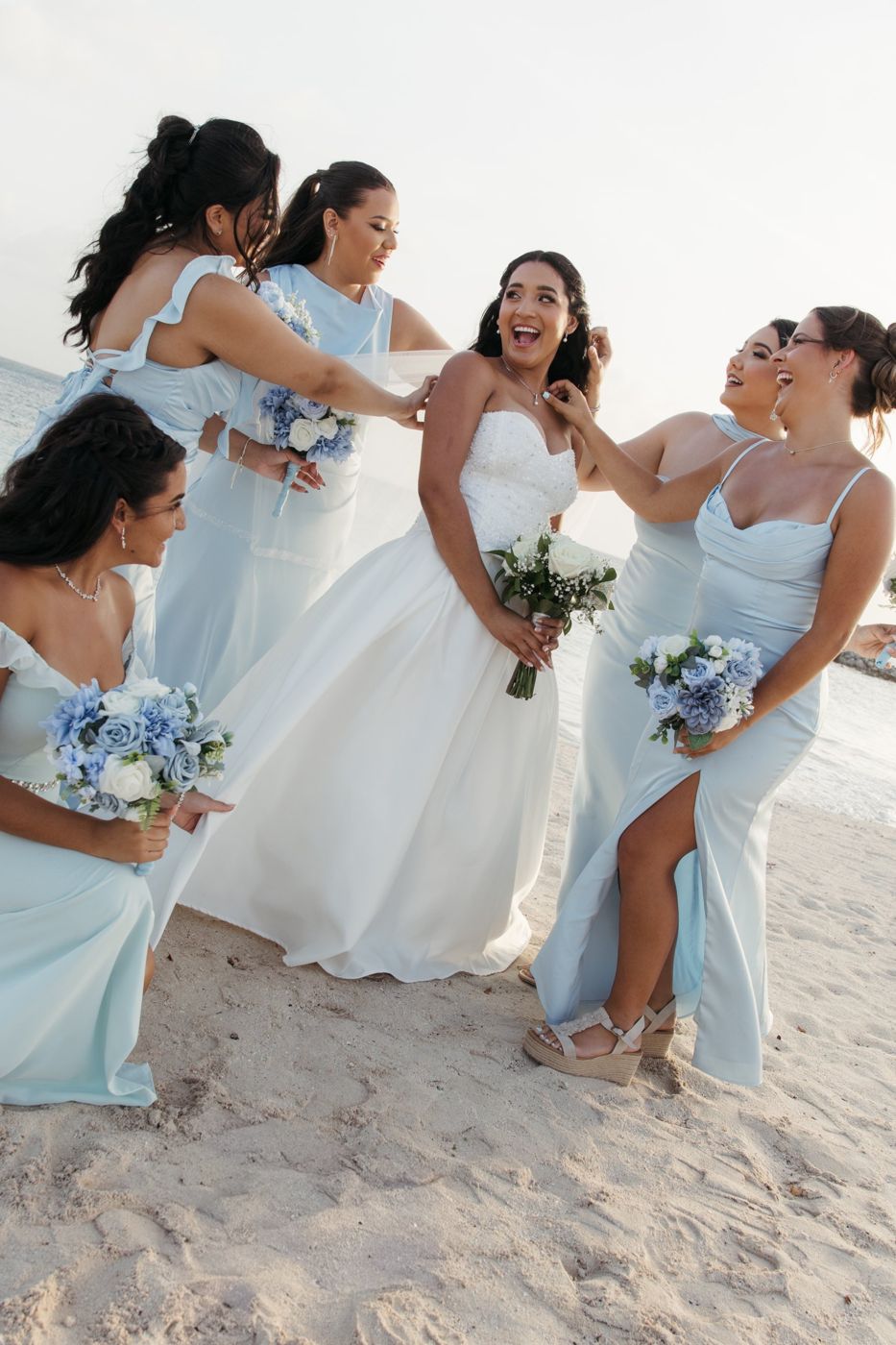 Laughing bride surrounded by bridesmaids in powder blue on the beach