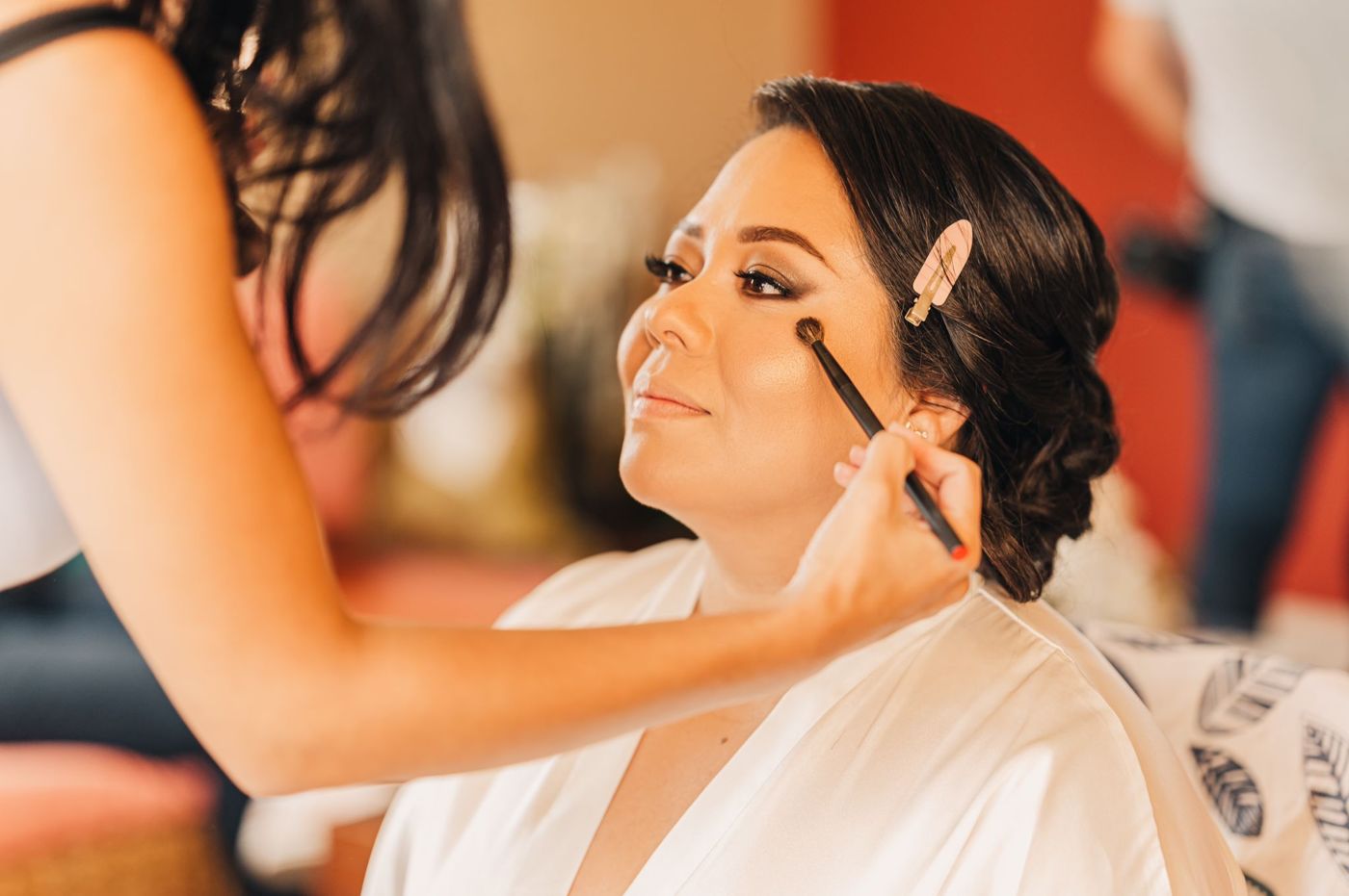 Smiling bride in a white robe while Pebbles finishes her makeup