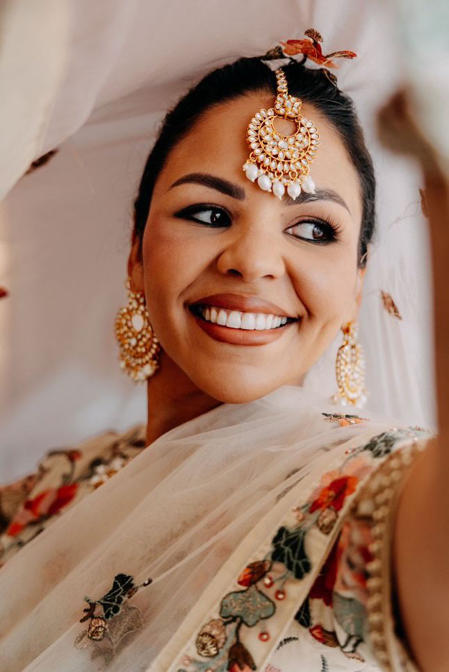 Smiling bride with a gold maang tikka under a sheer veil
