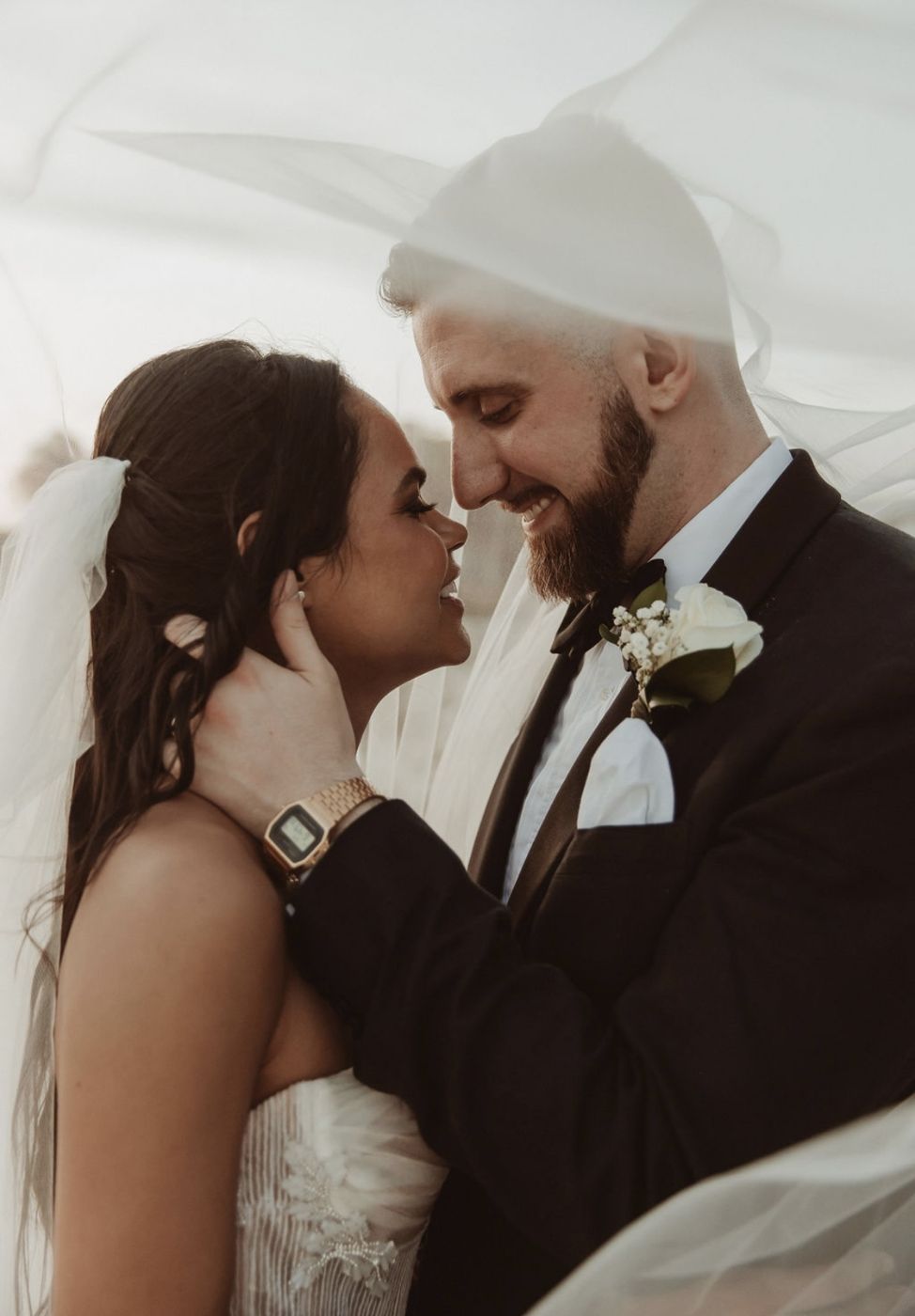 Bride and groom smiling nose to nose under her flowing veil